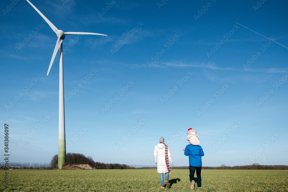 Back view of parents with little daughter walking on a field with wind wheel in the background Back view of parents with little daughter walking on a field with wind wheel in the background
