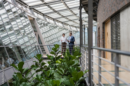 Businessman and woman talking in sustainable office building, using digital tablet photo
