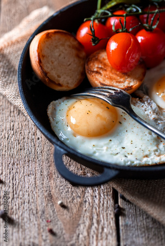 Fried eggs in a pan with cherry tomatoes and bread for breakfast. Breakfast concept. Wood background.