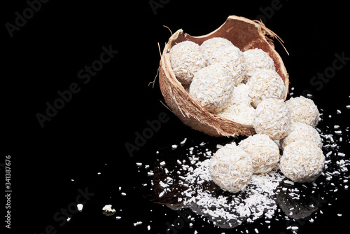 White coconut balls, raw and healthy sugar free rafaello candies on black glass background. Covering balls in coconut shred. Vegan, vegetarian sweets photo