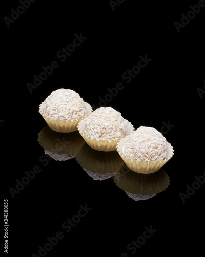 White coconut balls, raw and healthy sugar free rafaello candies on black glass background. Covering balls in coconut shred. Vegan, vegetarian sweets photo