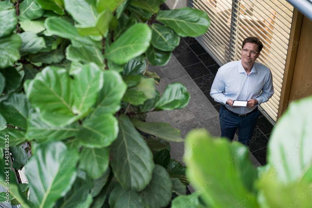 Businessman standing in sustainable office building, holding digital tablet Businessman standing in sustainable office building, holding digital tablet