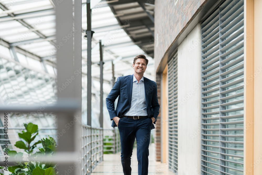 Confident businessman walking on gallery of green atrium Confident businessman walking on gallery of green atrium
