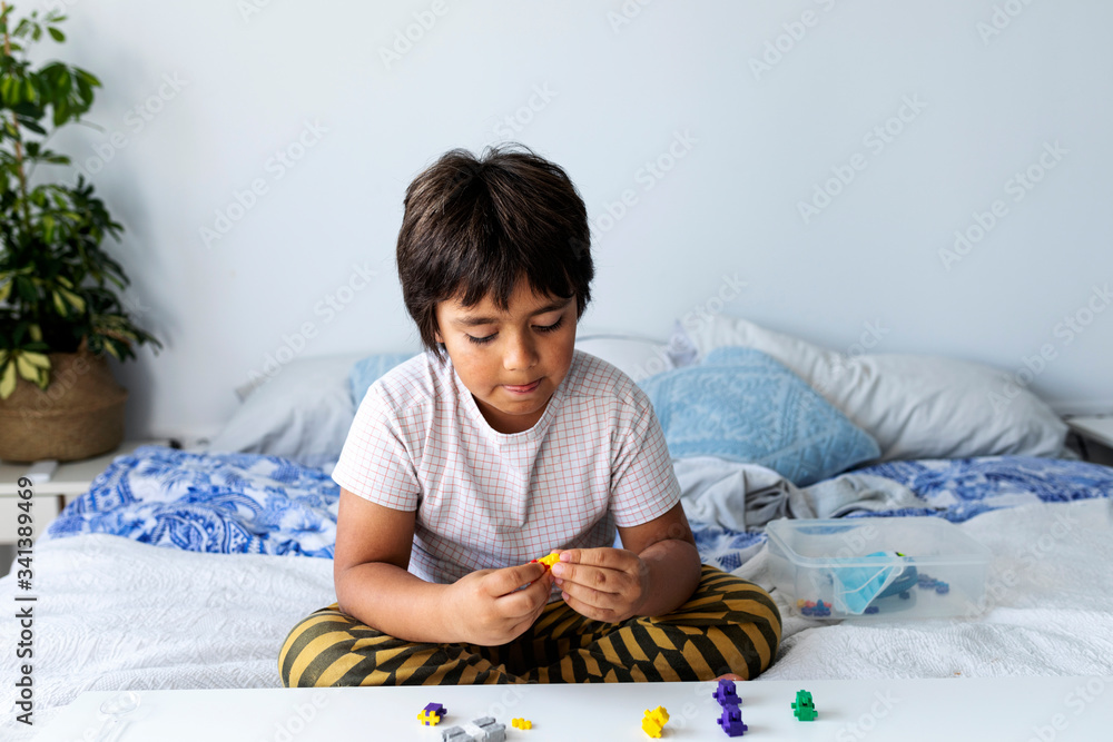 Boy sitting on bed playing with building blocks Boy sitting on bed playing with building blocks