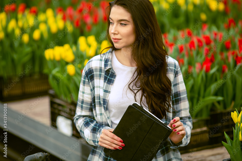Obraz premium Girl worker, Beautiful young smiling girl with tablet, worker with flowers in greenhouse. Concept work in the greenhouse, flowers. Copy space stock image