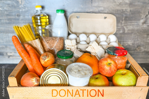 Donation volunteer box with various products for poor or elderly people on wooden background. Pandemic coronavirus food shortages. Food donations or delivery concept. Free space for text copyspace