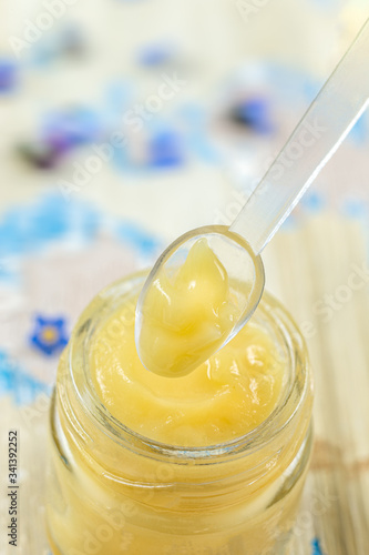 Raw organic royal jelly in a small bottle with litte spoon on small bottle on flower background, photo