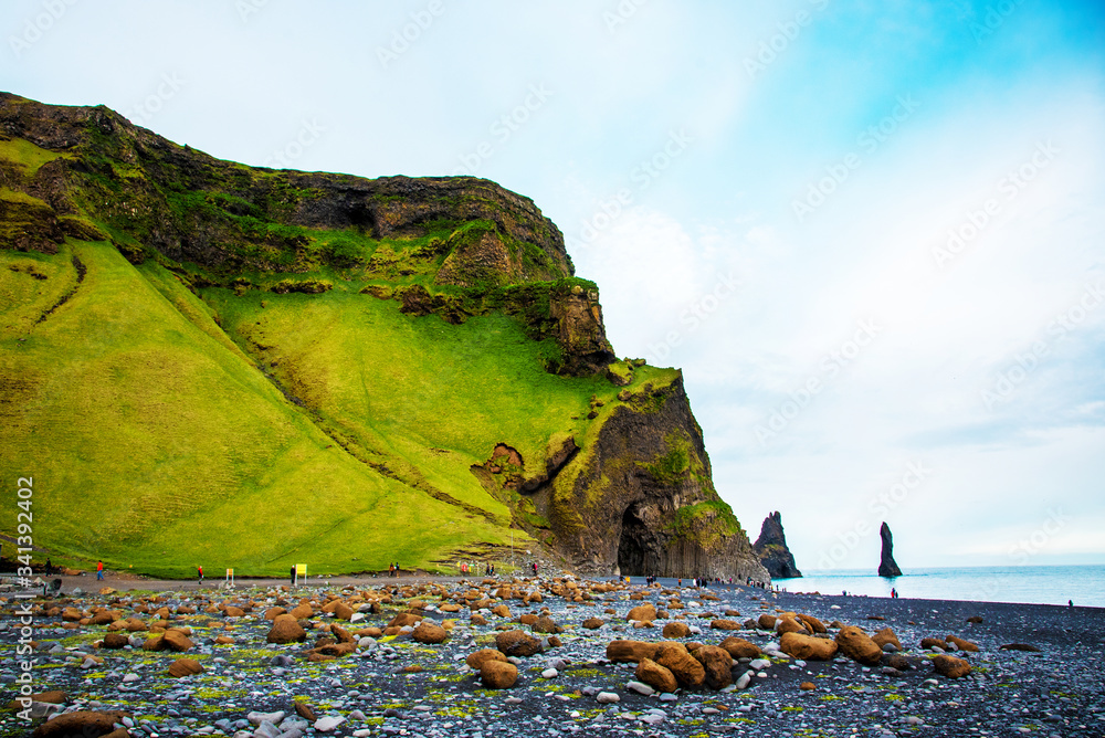 Beautiful dramatic landscape with cave in basalt rock on the black sand beach on Reynisdrangar Sea Cliffs, stones called Troll under the Reynisfjall Mountain near Vik, Iceland. Exotic countries.