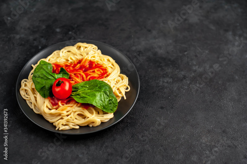 
Italian pasta spaghetti with tomato sauce and herbs on a black plate on a stone background with copy space for your text