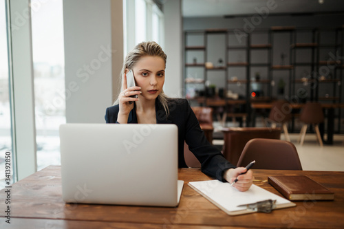 A young girl-Manager, sitting in a coworking office at her workplace in front of an open laptop, and naznaechet on the phone business meeting
