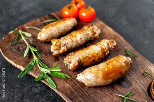 Grilled sausages with spices, tomatoes, rosemary on a stone background