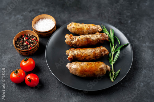 Grilled sausages with spices, tomatoes, rosemary on a stone background