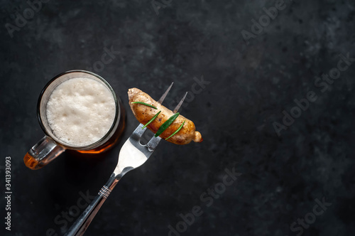 Beer and grilled sausage on a fork with spices on a stone background with copy space for your text