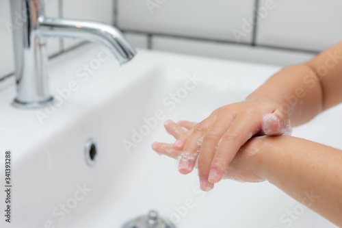 Kid washing hands in a white basin with a bar of white soap.
