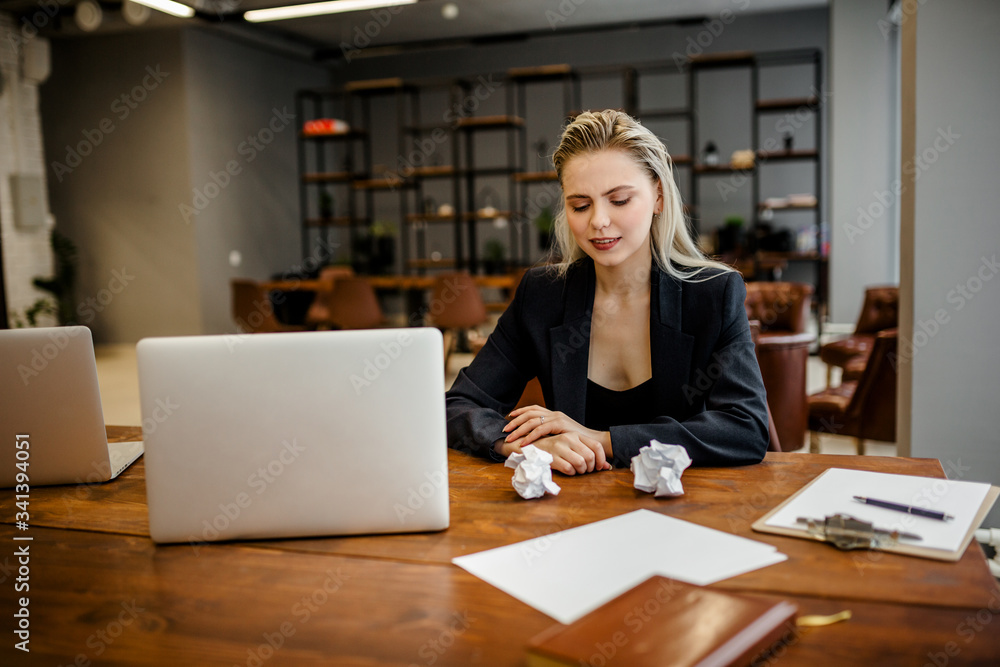 Obraz premium A beautiful businesswoman sits in the office and smiles hysterically because of the constant alterations in the reports