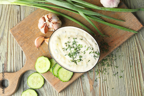 Delicious yogurt sauce with cucumber in bowl on wooden table