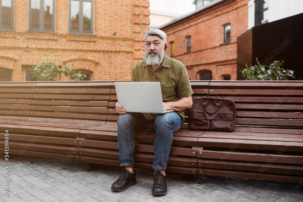A gray-haired businessman, sitting in a Park, slowly and alone working on his laptop