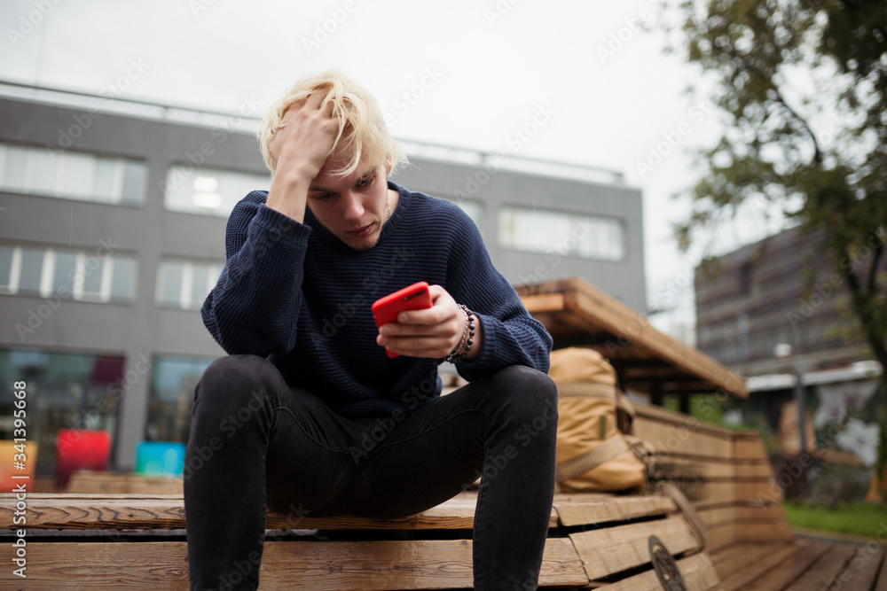 A young guy is sitting in a Park, holding his head in confusion, because he was abandoned by a girl online by correspondence in a chat A young guy is sitting in a Park, holding his head in confusion, because he was abandoned by a girl online by correspondence in a chat