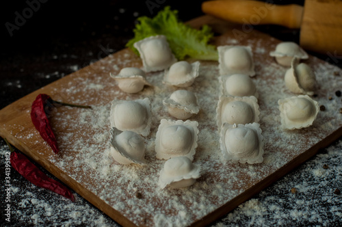modeling homemade Italian dumplings or ravioli on a dark background with scattered flour, a wooden rolling pin on the table and chili pepper