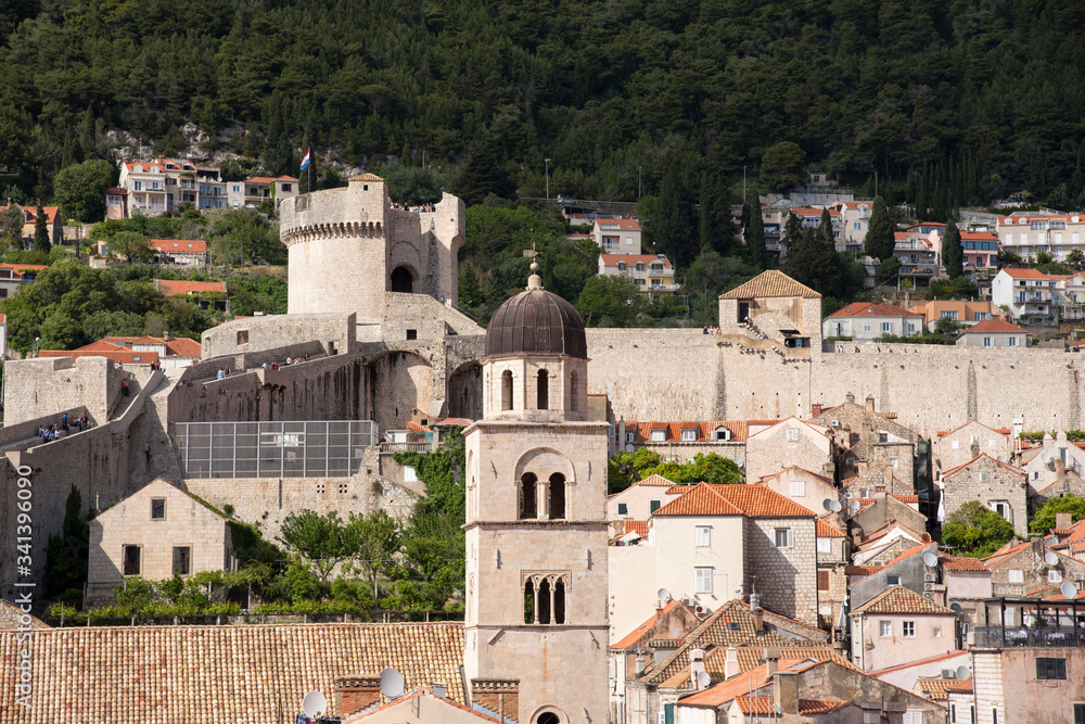 View of the red tile roofs, a tower and part of the stone wall, from a street in the upper part of the city, in Dubrovnik, Croatia, Europe.