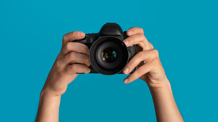 Closeup of photographer pointing DSLR camera at screen, blue background. Panorama