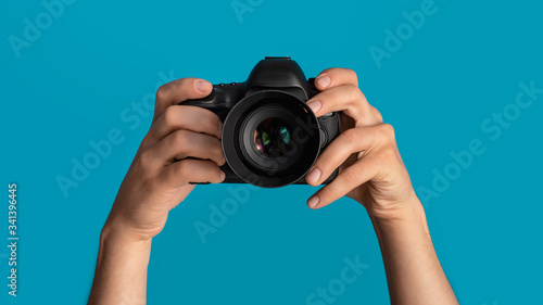 Closeup of photographer pointing DSLR camera at screen, blue background. Panorama photo