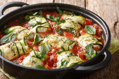 Hot appetizer of zucchini rolls baked with ricotta cheese and herbs in tomato sauce in a pan on the table. horizontal