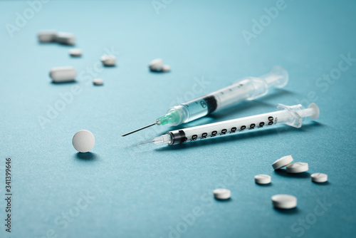 Two syringes with needles pointing to a round tablet among other tablets or medicine pills on a green surface. Perfect for flu, epidemic, pandemic, symptoms treatment, recovery or immunization.