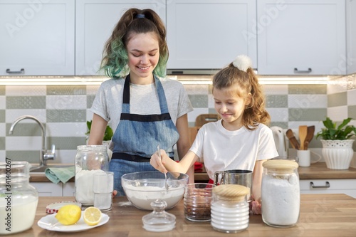 Two girls, teenager and younger sister, preparing cookies together in kitchen