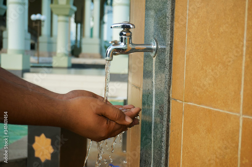 A moslem man take ablution, known as wudhu, as one of ritual purification to pray : washing hand.  Outside mosque.                               photo