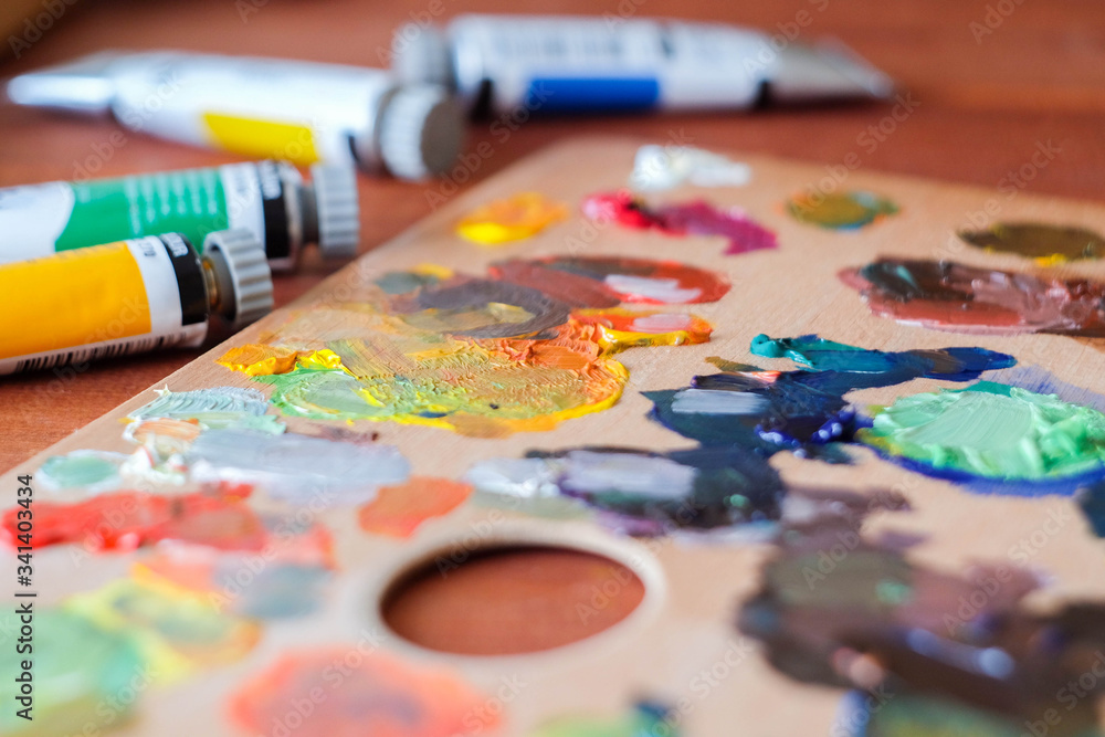 Fototapeta premium Close up oil painting process. Oil paints palette. Oil painting tools on the wooden table. Painter work place. Paint tubes.