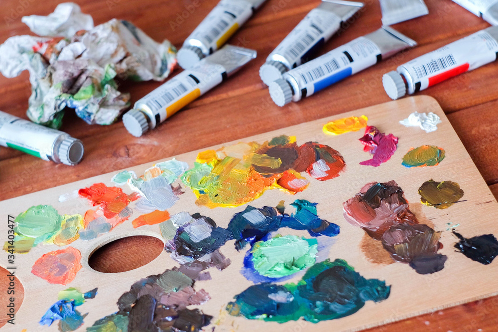 Close up oil painting process. Oil paints palette. Oil painting tools on the wooden table. Painter work place. Paint tubes. Close up oil painting process. Oil paints palette. Oil painting tools on the wooden table. Painter work place. Paint tubes.