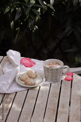 White porcelain cup of hot coffee, cappuccino with three Italian amaretti cookies.Summer breakfast in a terrace - coffee, amaretti and flowers