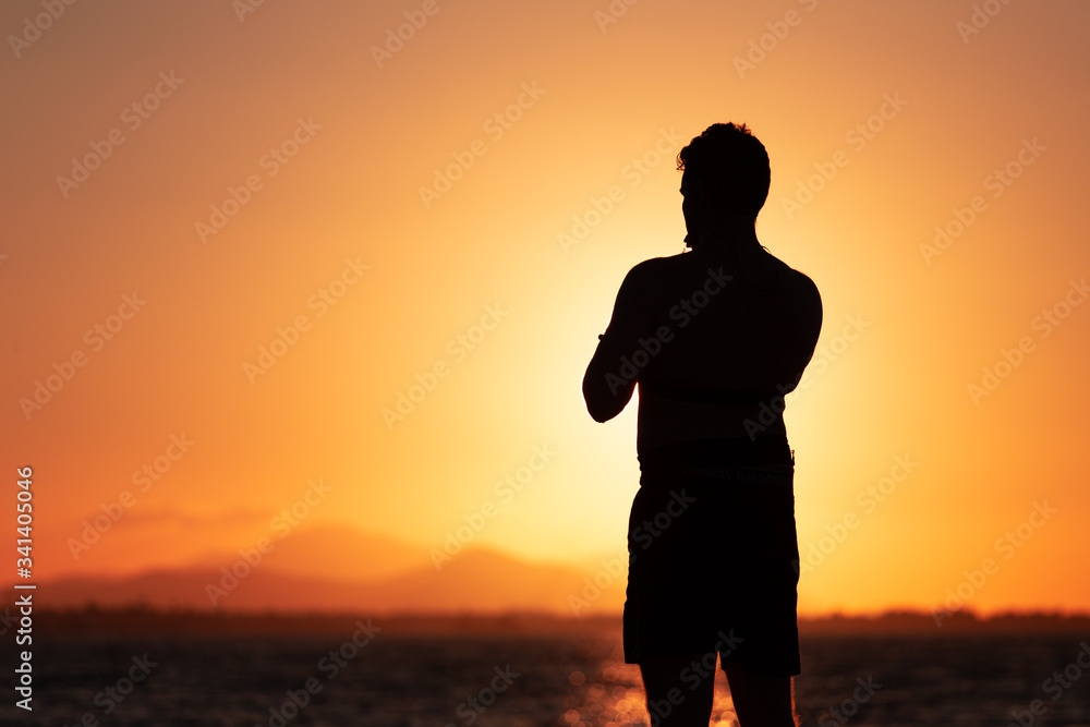Silhouette of a guy standing in front of a sunset while during exercise.
