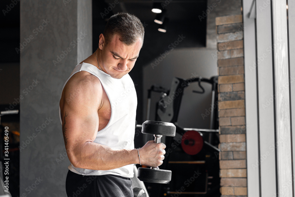 Fitness instructor doing biceps exersices with dumbbell in gym around fitness equipment. Fitness instructor doing biceps exersices with dumbbell in gym around fitness equipment.