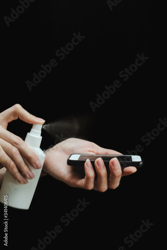 Male hand with a sanitizer spray disinfect the surface of the smartphone on black background. Covid-19 Coronavirus Quarantine Pandemic. Isolation at home. Protect yourself and your loved ones. © tumana_net