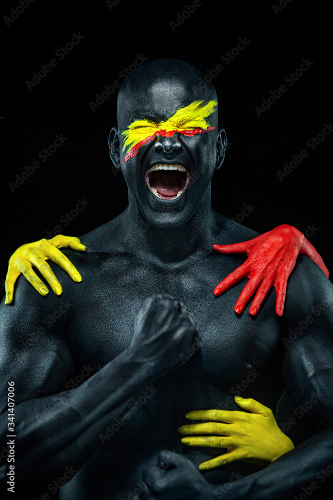 Man with female hands on the body. Bodybuilder athlete with yellow face art and body paint. Colorful portrait of the guy with bodyart.