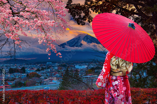  Asian women wear Japanese kimonos. Holding a red umbrella at Mount Fuji and cherry blossoms in Japan.