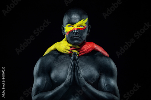 Fototapeta Naklejka Na Ścianę i Meble -  Man with female hands on the body. Bodybuilder athlete with yellow face art and body paint. Colorful portrait of the guy with bodyart.