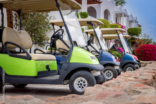 Several Golf cars are parked in the Parking lot. Electric cars for moving around the resort complex of a five-star hotel. A means of transportation for tourists.