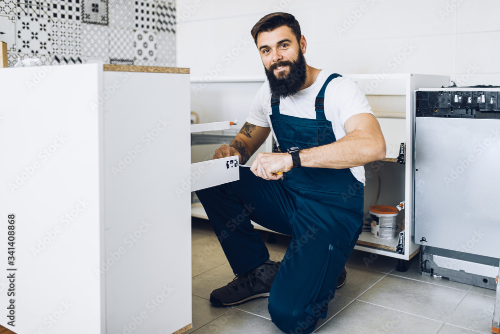 Young bearded handyman working in the kitchen. Renovation.