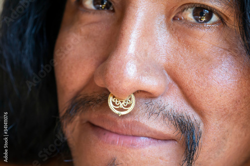 Portrait of young hispanic man with long hair wearing a metal septum piercing at his nose