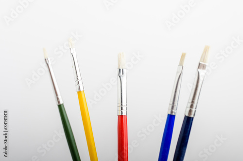 Five professional artist paintbrushes displayed horizontally isolated on a white studio paper, photographed with soft focus 