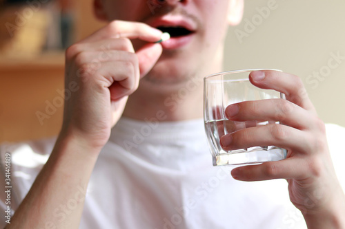 young man in a white T-shirt drinks a capsule for treatment with water