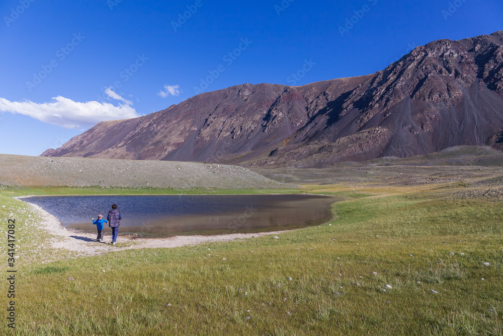 Father and son are walking along the grass near the mountain lake of the Mongolian Altai
