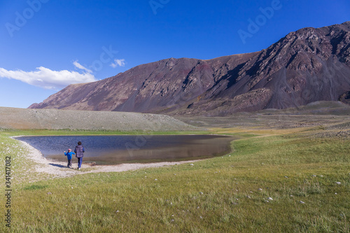 Father and son are walking along the grass near the mountain lake of the Mongolian Altai