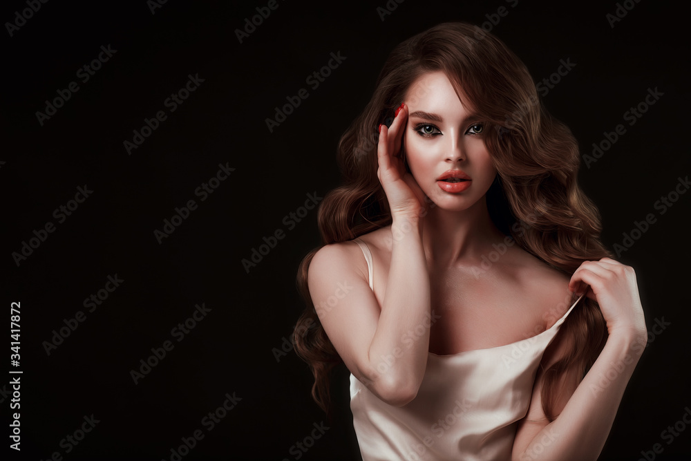 Naklejka premium Beauty portrait of elegant young woman. Glamour makeup. Face of the beautiful woman with long brown curly hair posing at studio over dark background. Sensual portrait.