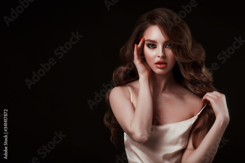 Beauty portrait of elegant young woman. Glamour makeup. Face of the beautiful woman with long brown curly hair posing at studio over dark background. Sensual portrait.