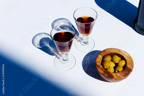 Two glasses of Sherry/fortified wine with bowl of olives on white. Hard shadows.
