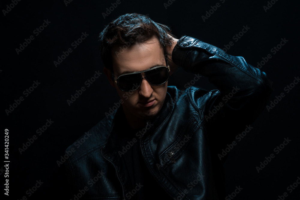 Obraz premium Young sexy stylish guy with glasses in a black leather jacket on a black background
